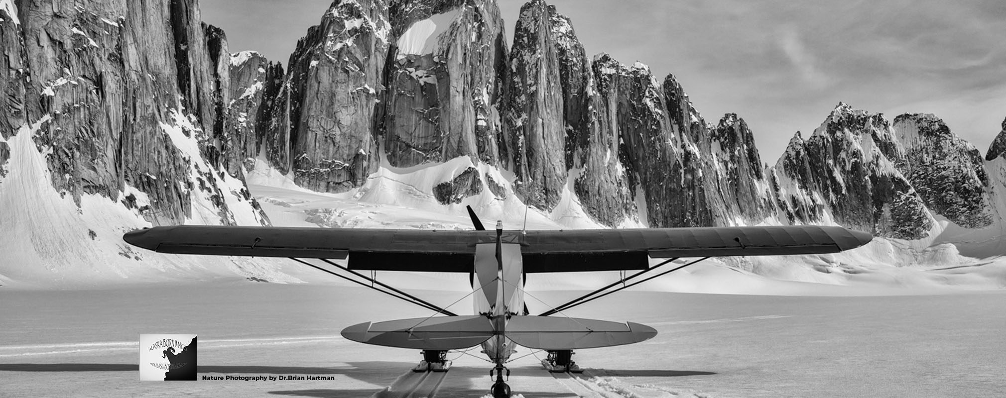 A ski-equipped bush plane parked before a glacier and jagged mountain range in Alaska